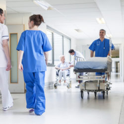 Male nurse pushing stretcher gurney bed in hospital corridor with doctors & senior female patient